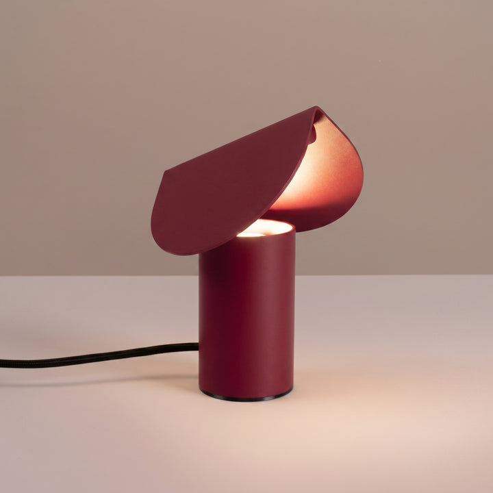Lampe à poser BISCUIT bordeaux allumée, sur une table