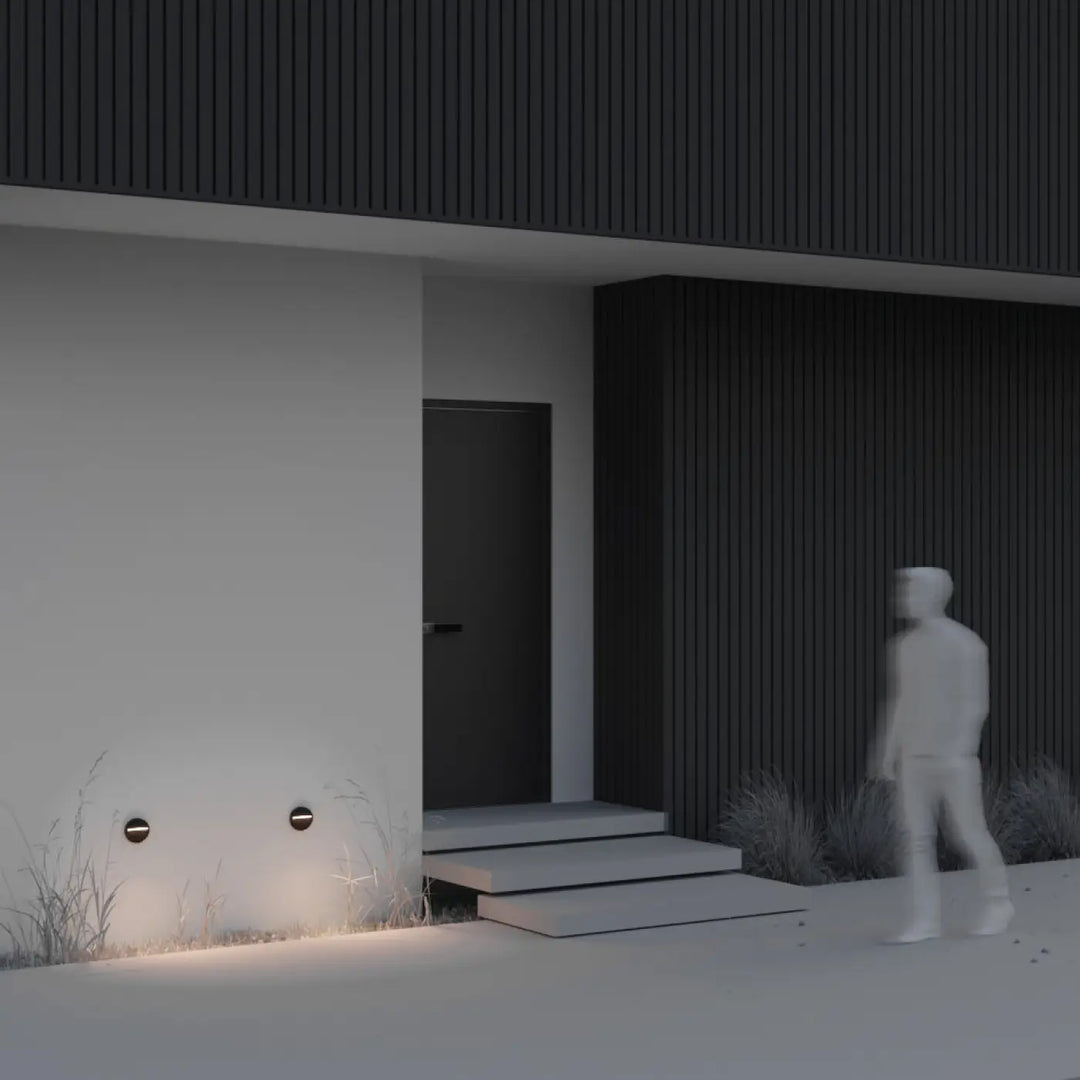 Applique extérieure balise ronde noire minimaliste avec lumière douce éclairant la base d’une maison moderne