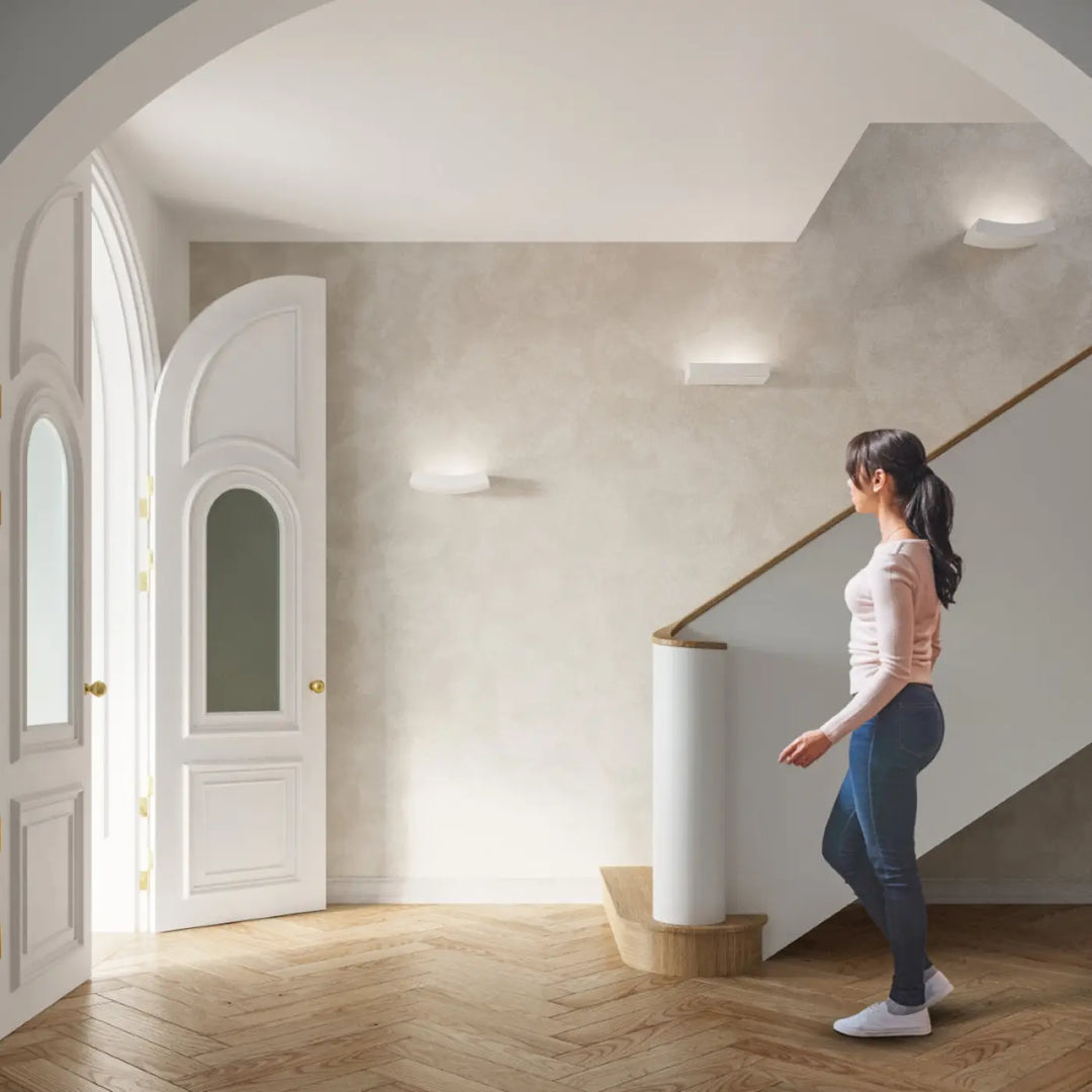 Une femme en haut rose clair et jean bleu foncé se tient près d une applique murale hattor en céramique créant une ambiance unique