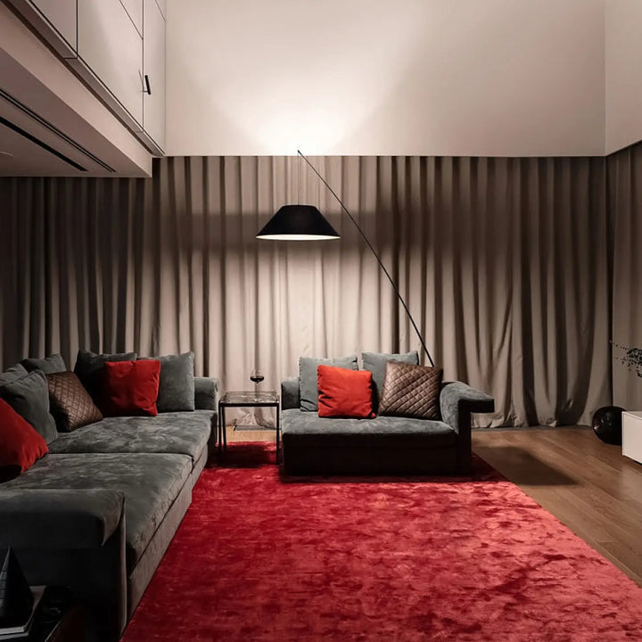 Lampadaire arc avec tige télescopique près d’un canapé sectionnel en velours tissu noir avec coussins rouges et marron