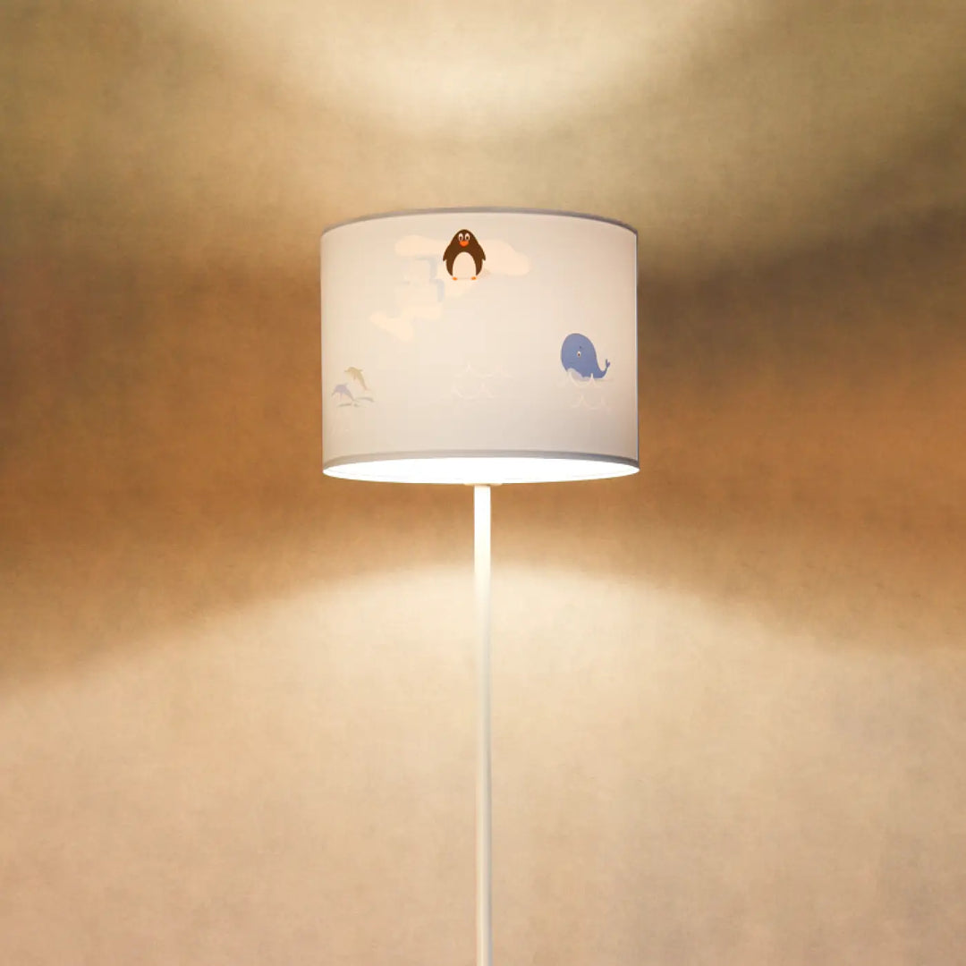 Lampadaire enfant bleu avec abat-jour cylindrique blanc illustré de pingouin et baleine sur pied fin blanc