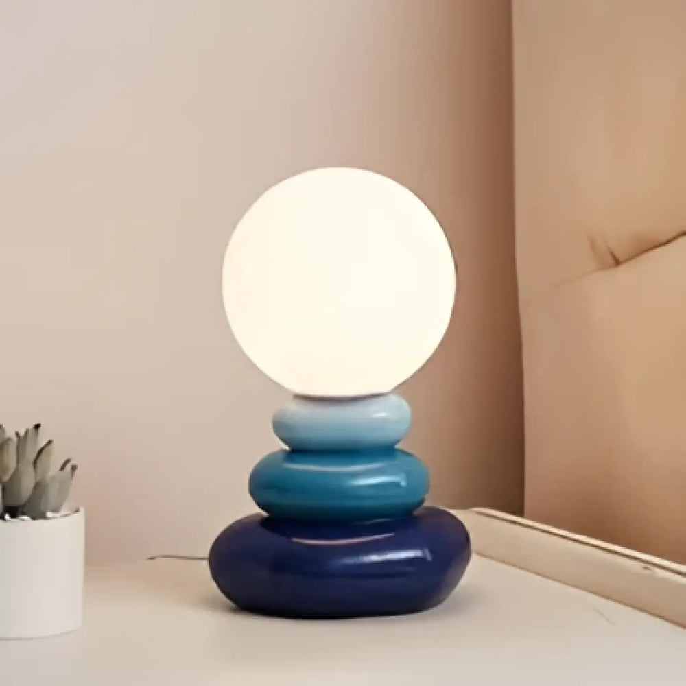 Lampe de chevet hestia avec design galets empilés et base circulaire bleue surmontée dune sphère lumineuse blanche