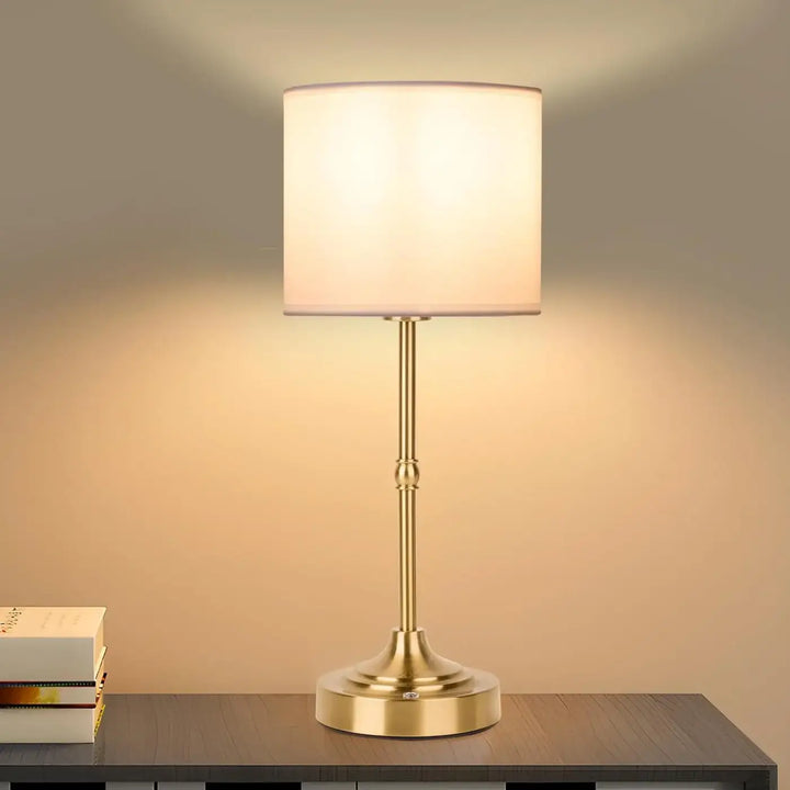 Lampe de chevet élégancia en or brossé avec abat-jour cylindrique en tissu blanc design élégant et chevet contemporaine