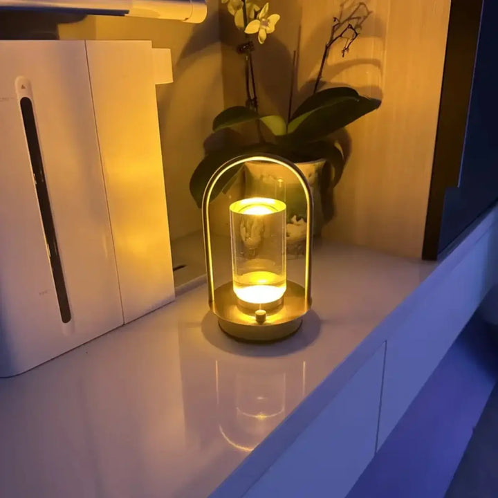 Lampe de table neora avec arche épurée en métal doré et lumière cylindrique flottante émise par un verre clair