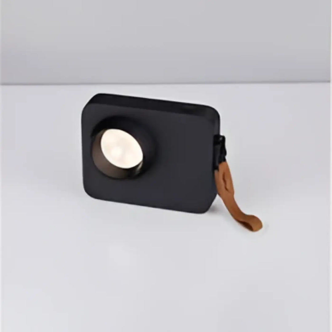 Lampe de table focalis avec faisceau lumineux ciblé, enceinte portable noire, grille blanche circulaire et sangle cuir marron
