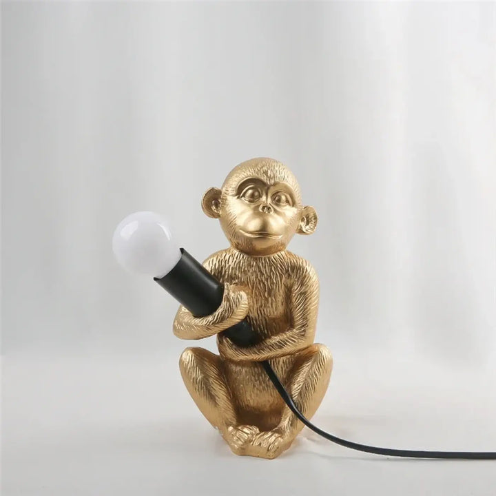 Lampe de table zaboo singe assis en métal texturé doré tenant une ampoule à poignée noire sculpturale singe assis