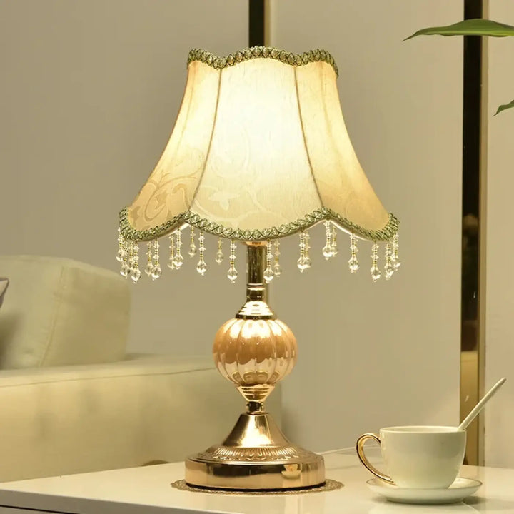 Lampe de table gold ton avec abat-jour en tissu crème à franges en cristal et base métallique ornée pour décoration intérieure vintage chic