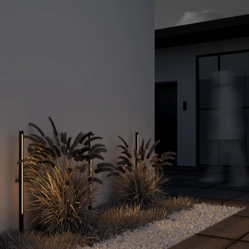 Poteau lumineux noir slim led avec blanc chaud monté verticalement à côté de graminées ornementales en trois hauteurs