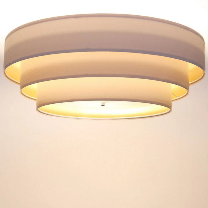 Plafonnier rond blanc doré triniti veloursstoff avec trois abat-jours circulaires en tissu beige émettant une lumière chaude