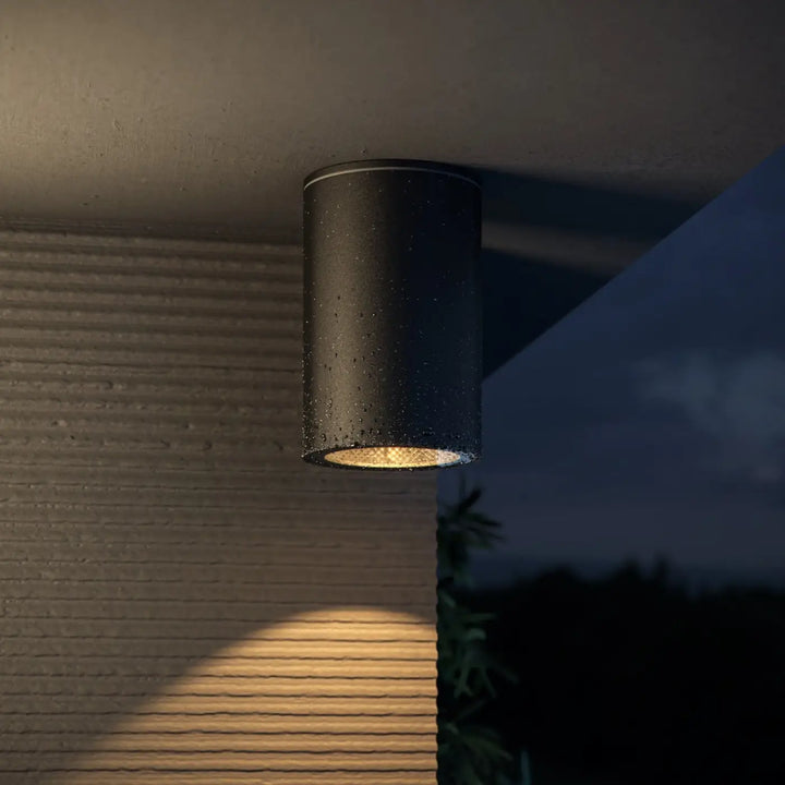 Spot roll cylindre noir en acier noir avec finition mate tachetée et lumière dorée chaude émise par le bas ouvert