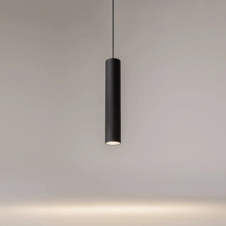 Suspension artisan noire cylindrique avec surface texturée et lumière chaude idéale au-dessus d’une table
