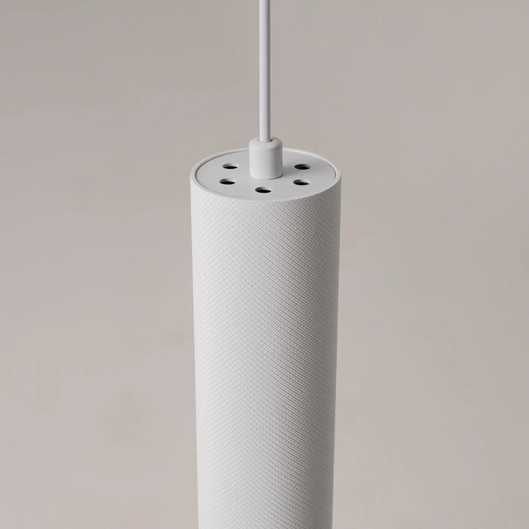 Suspension artisan blanche cylindrique en tissu texturé avec trous de ventilation au-dessus d’une table