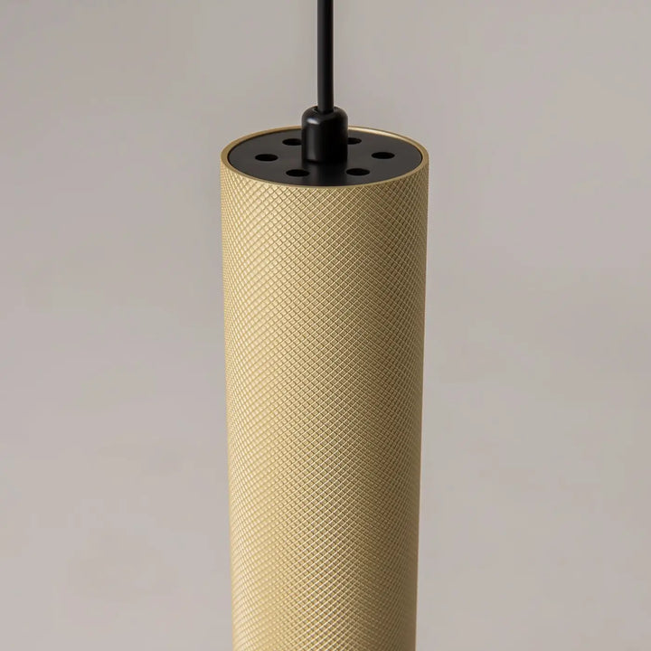 Suspension artisan cylindrique dorée au-dessus d’une table avec surface texturée en losanges et chapeau noir perforé