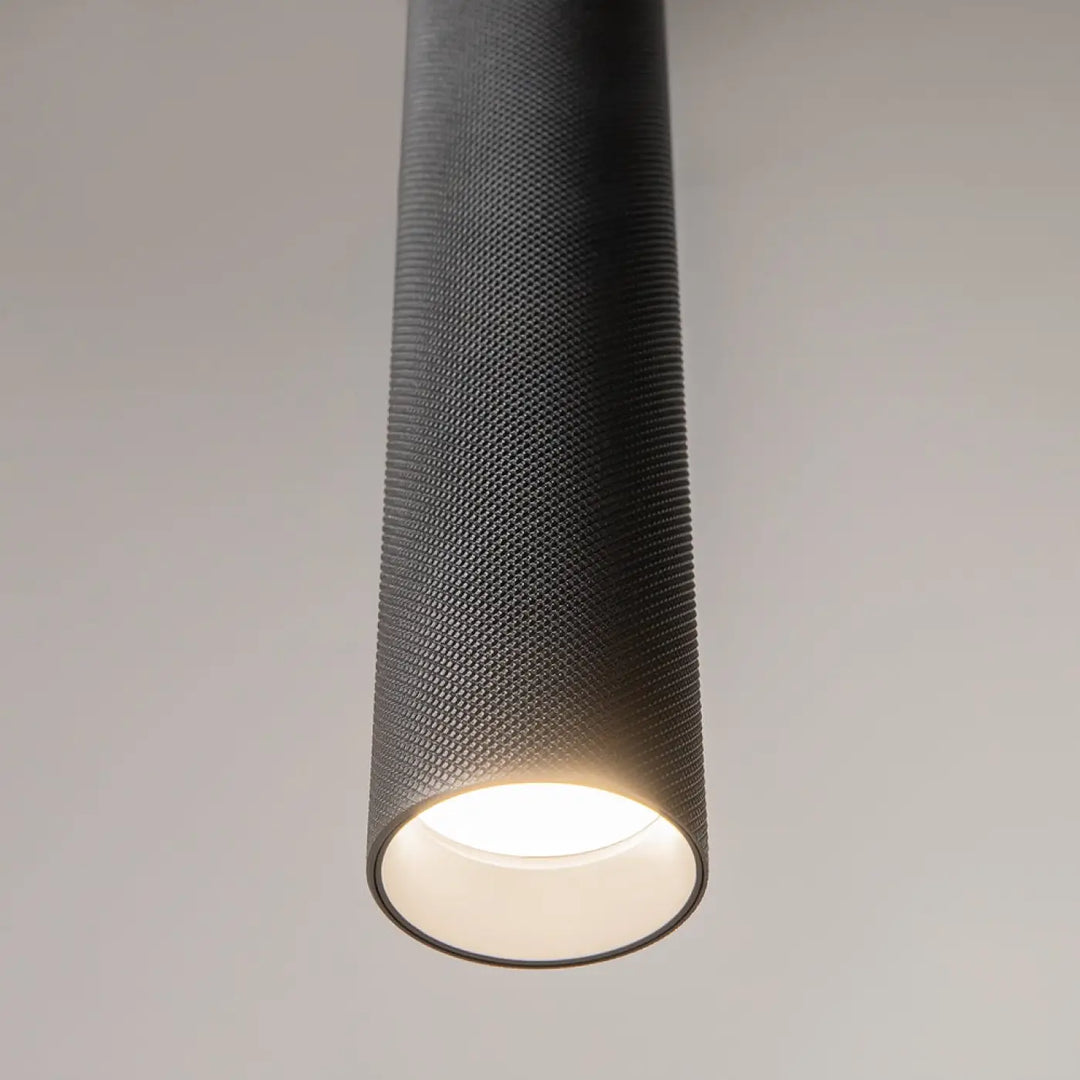Suspension artisan noire cylindrique avec finition mate texturée et éclairage led blanc chaud au-dessus d’une table