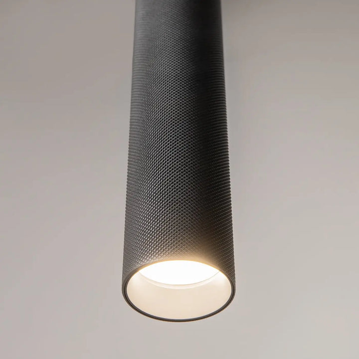 Suspension artisan noire cylindrique avec finition mate texturée et éclairage led blanc chaud au-dessus d’une table