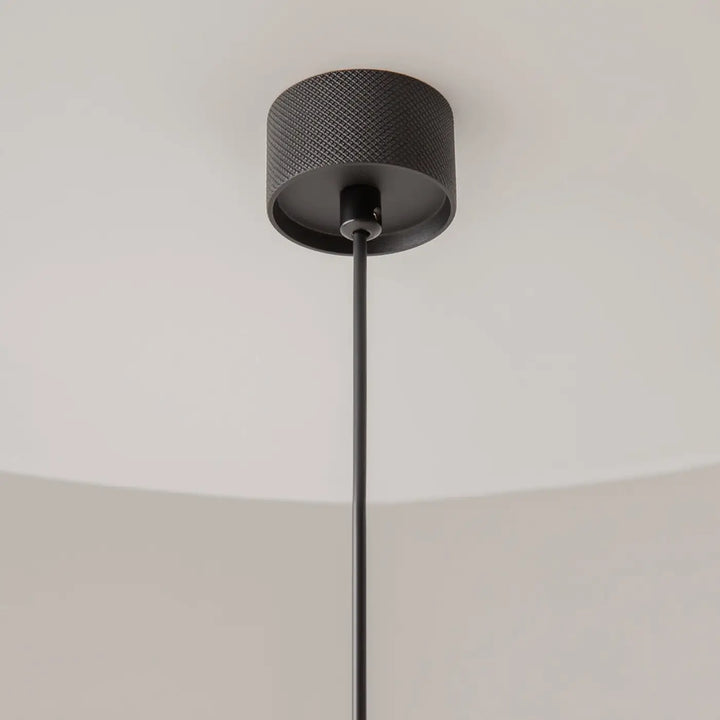 Suspension artisan au-dessus d’une table avec plafond noir texturé design cylindrique mat