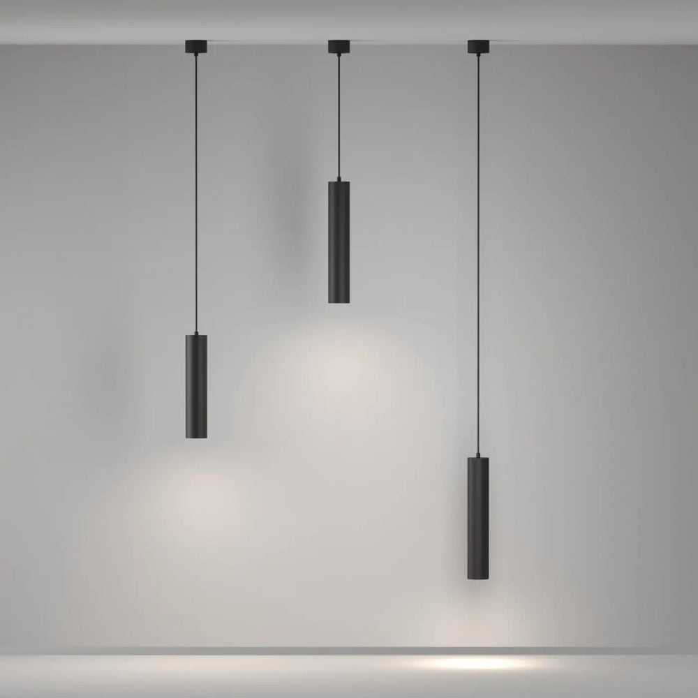 Suspension artisan avec trois luminaires cylindriques noirs au-dessus d’une table, design minimaliste et finition mate