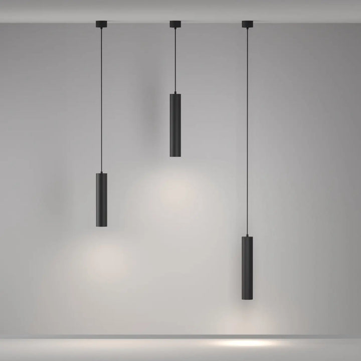 Suspension artisan avec trois luminaires cylindriques noirs au-dessus d’une table, design minimaliste et finition mate