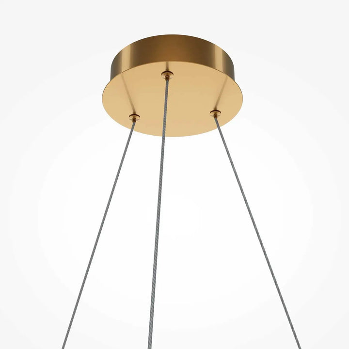 Suspension luminaire breeze anneau avec fixation plafond dorée et trois câbles gris en acrylique texturé au-dessus d’une table