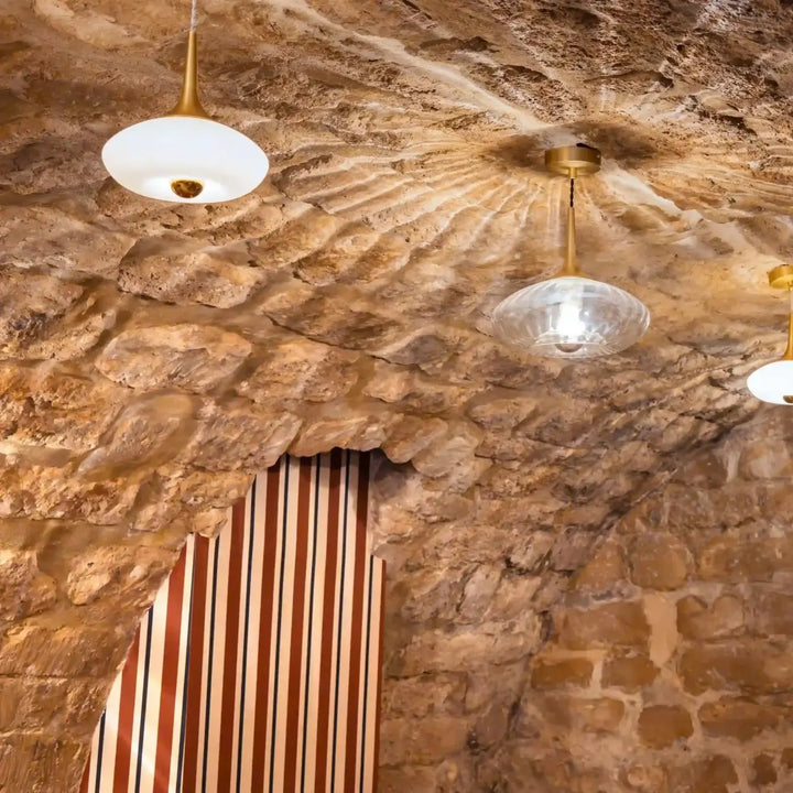 Suspension luminaire modèle grace en verre soufflé avec finitions dorées suspendue à un plafond en pierre rustique
