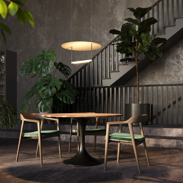 Suspension led ambiance au-dessus d’une table salle à manger ronde en bois avec base noire et chaises vertes