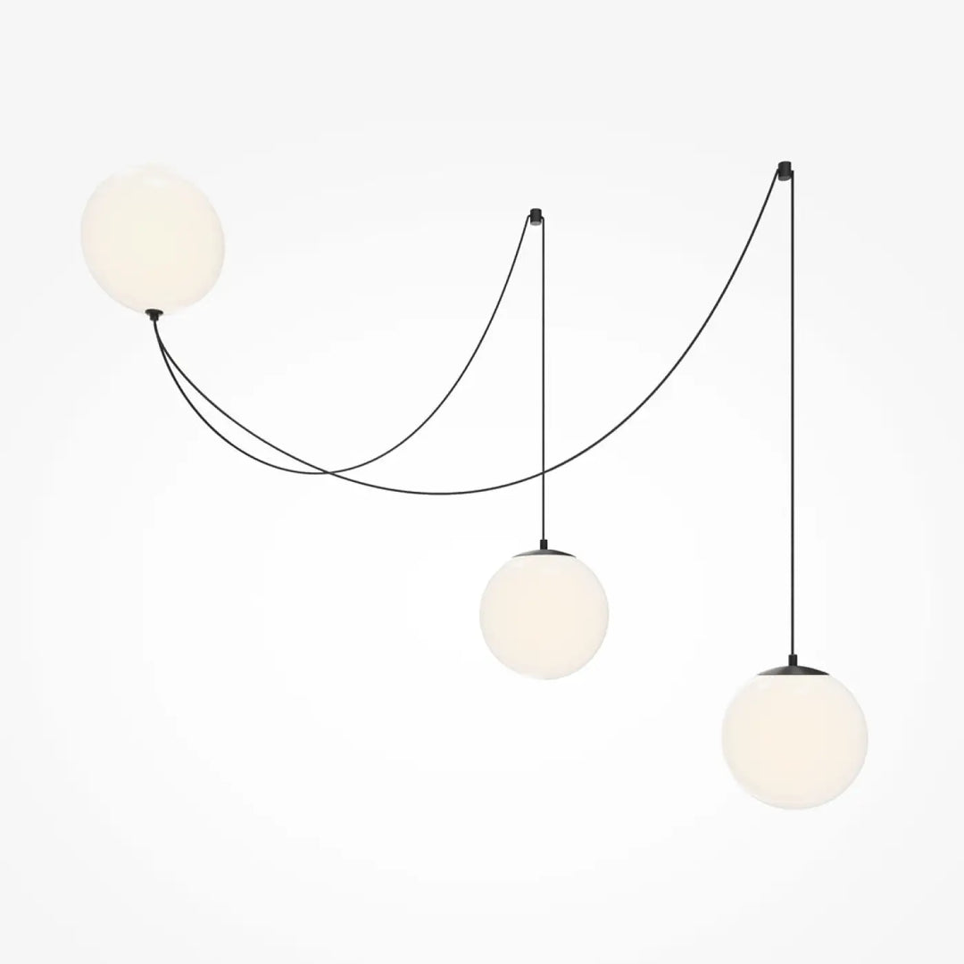 Suspension luminaire twins avec trois globes en verre dépoli blanc suspendus par des cordons noirs au-dessus d’une table