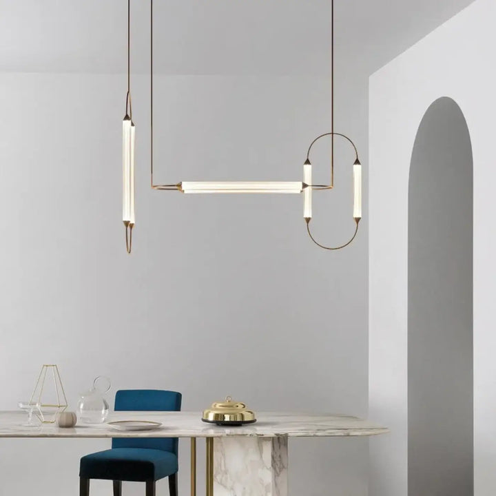 Suspension luminaire orsen avec sources lumineuses en tube de verre dépoli et cadre en laiton seul couleur au-dessus d’une table en marbre
