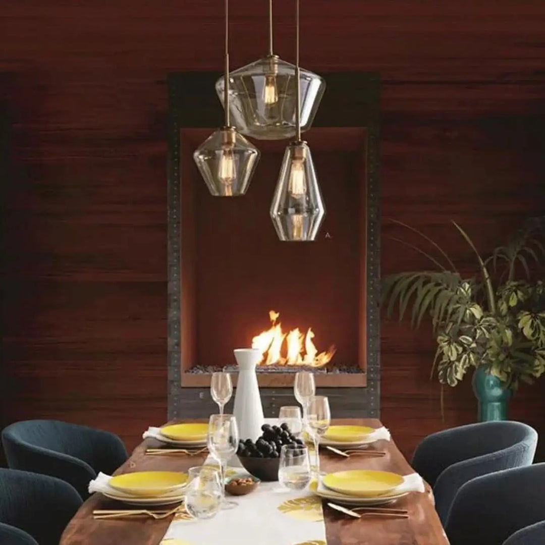 Suspension luminaire glazia avec trois abat-jours en verre transparent et métal doré suspendus au-dessus d’une table à manger