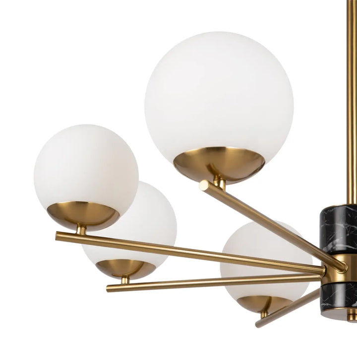 Suspension luminaire marble avec structure dorée, colonnes en marbre noir et quatre globes en verre dépoli au-dessus d’une pièce