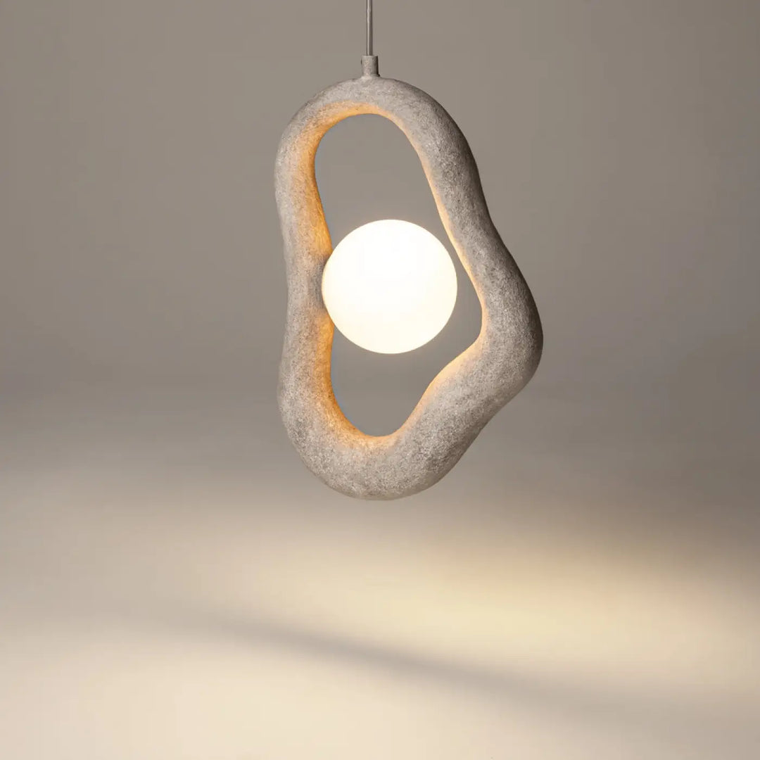 Suspension opus en béton gris avec cadre ovale à volume irrégulier et lumière douce émanant d’une ampoule sphérique blanche