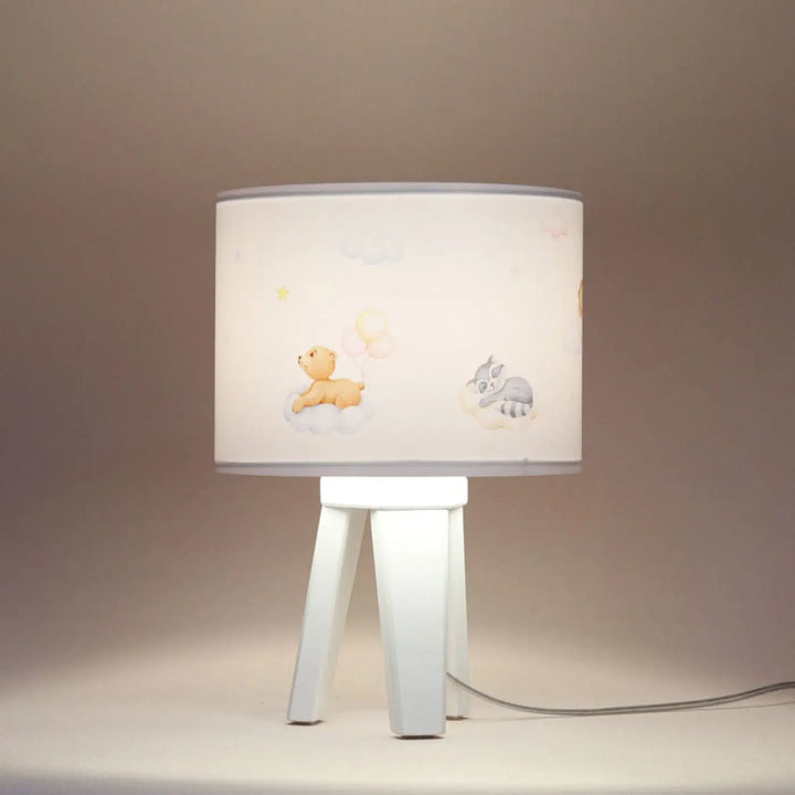 Lampe de table sweet dreams blanc avec abat-jour cylindrique illustré dours jaune et raton laveur gris sur socle trépied blanc minimaliste